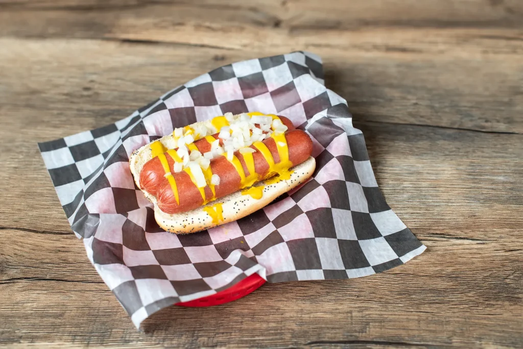 Staleys hotdog with a checkered wrapper placed on a wooden table.