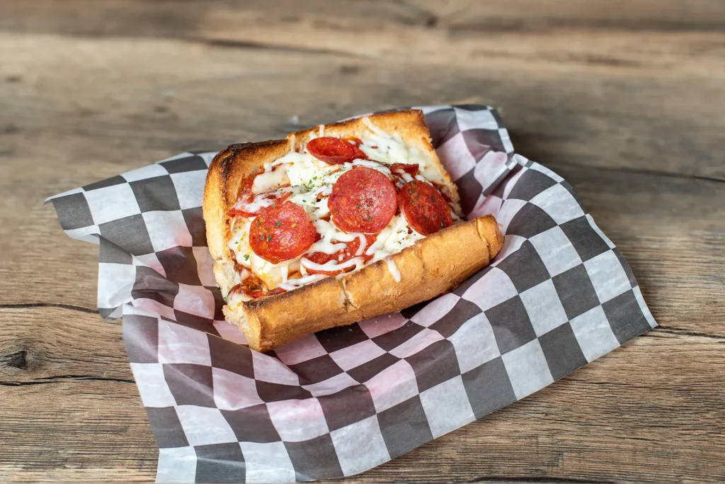 Staleys Midway Monster Meatball with Pepperonis with a checkered wrapper placed on a wooden table.