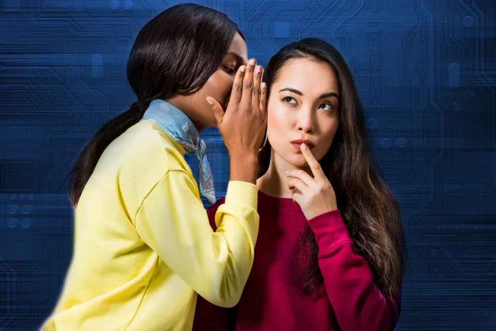 Two women whispering with computer motherboard behind them.